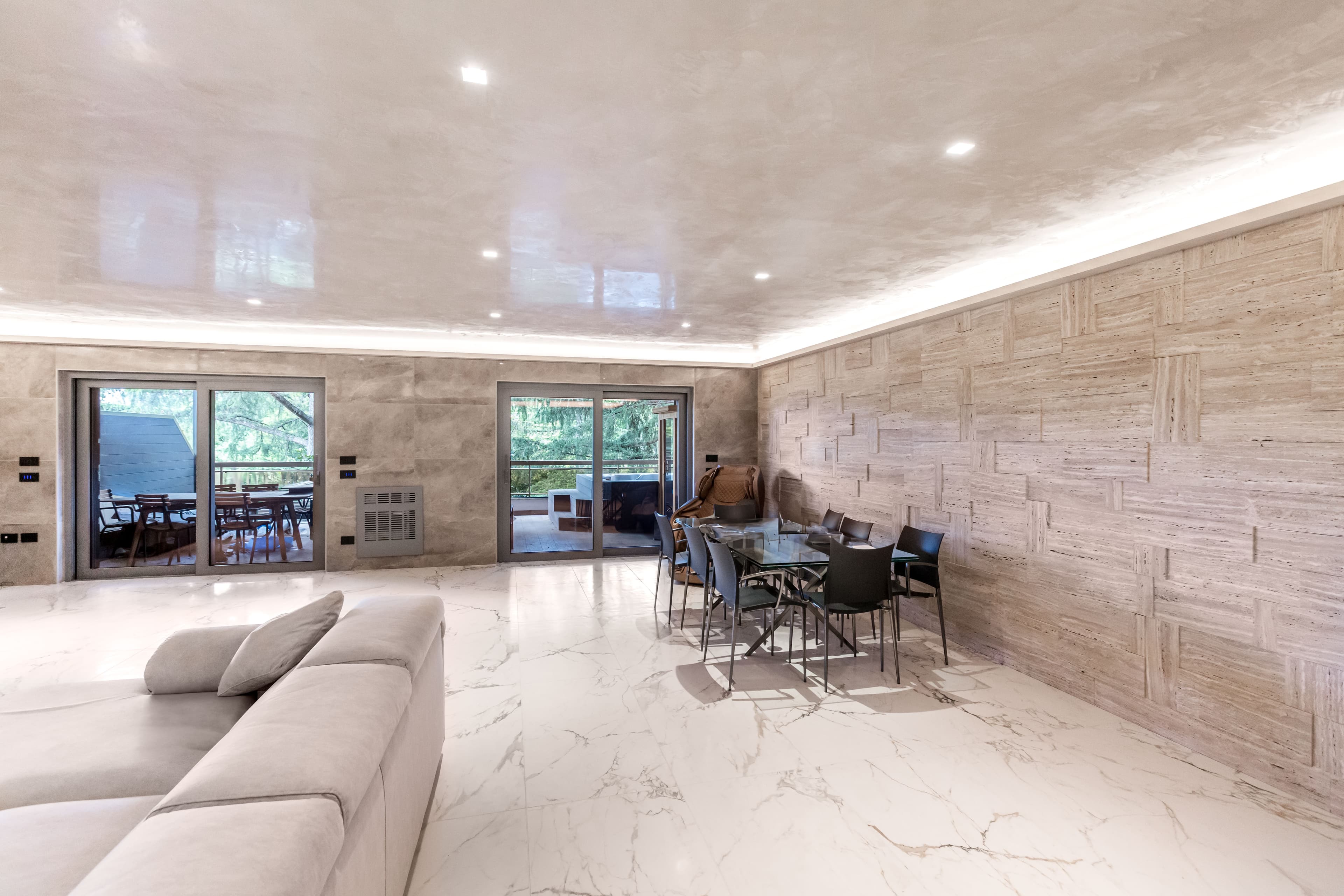 Ampio salone con pavimento in marmo, parete in travertino e vetrate sulla terrazza coperta